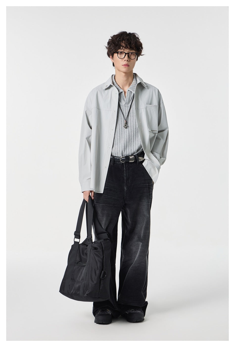 Full-length model wearing a light gray oversized shirt over a gray knit top and black wide-leg trousers.
