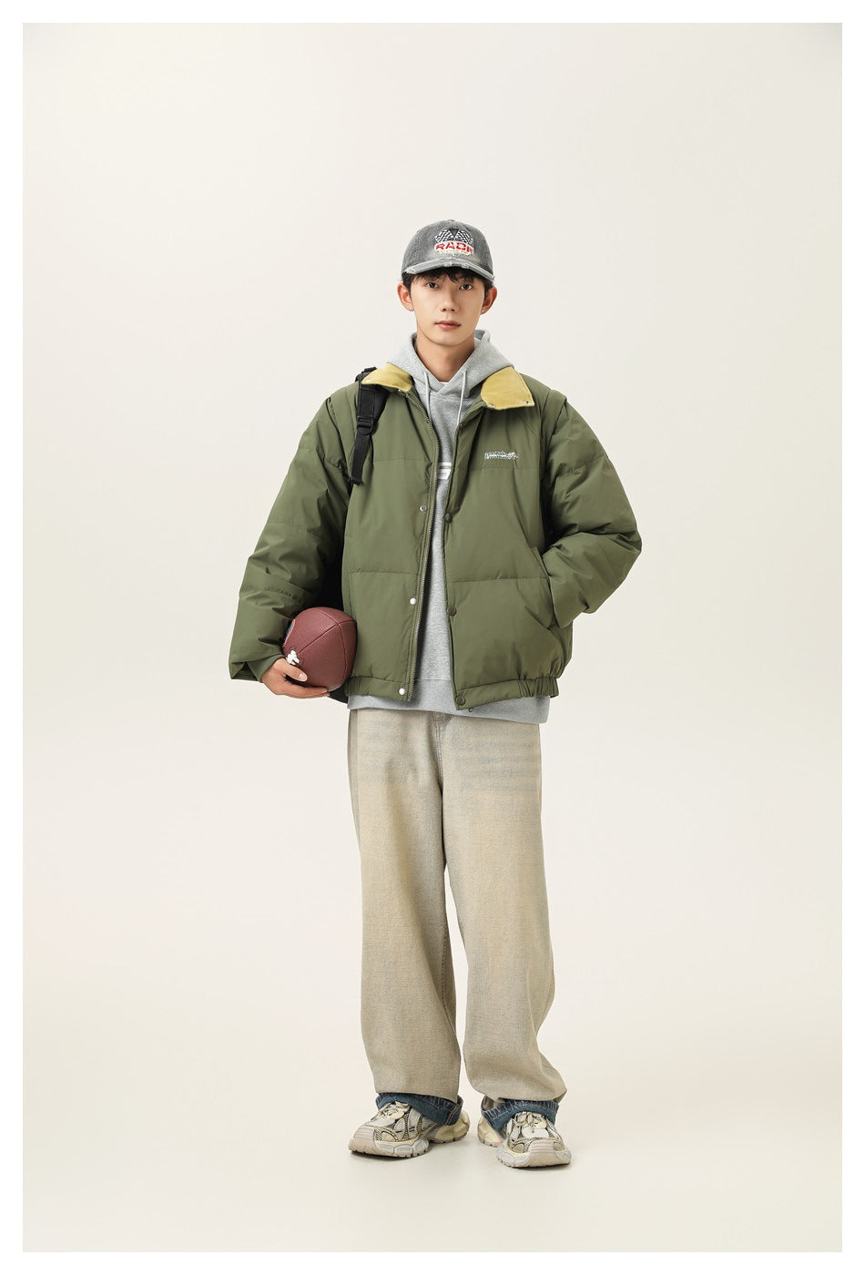 Model wearing an olive green puffer jacket with a mustard collar over a gray hoodie and wide beige pants