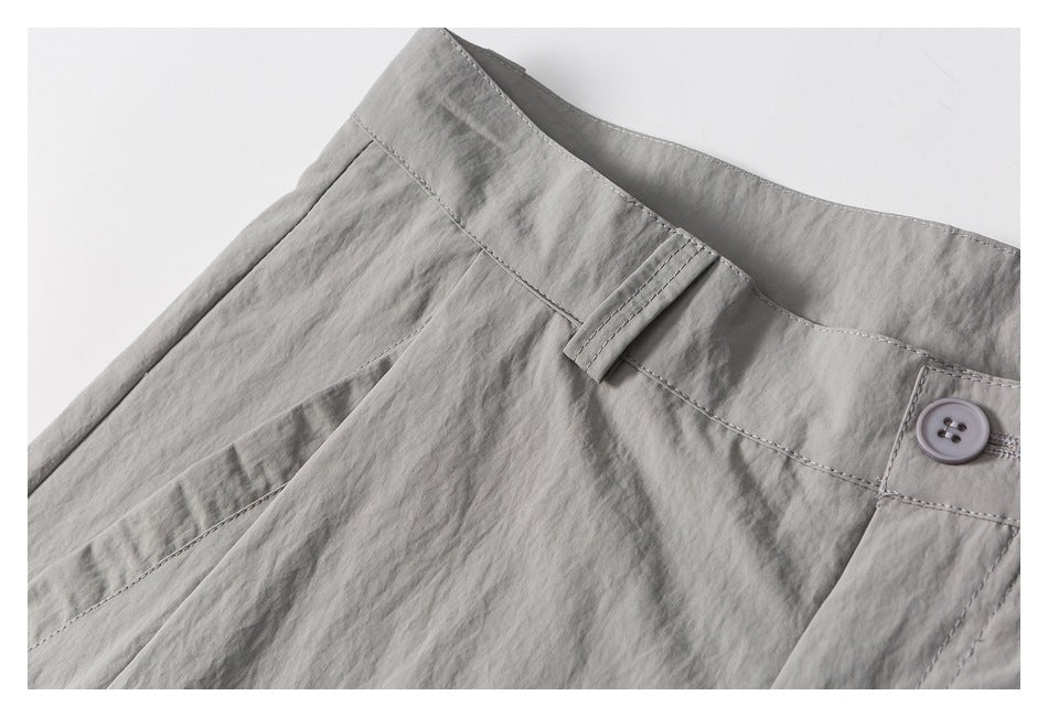 Close-up of gray trousers showing the waistband, button, belt loop, and front pocket.