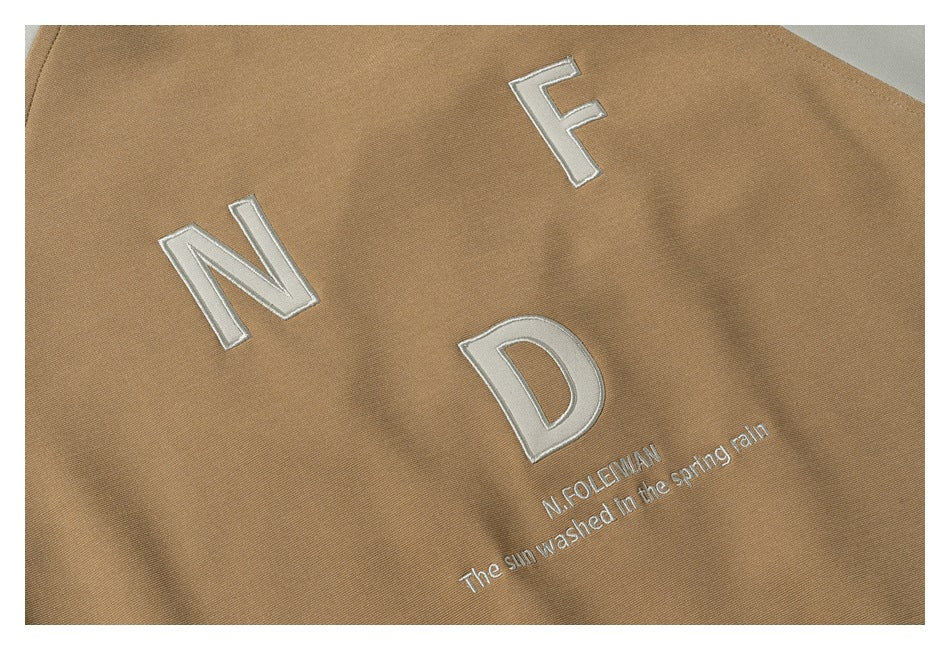 Close-up of white embroidered letters and small text on tan garment fabric.