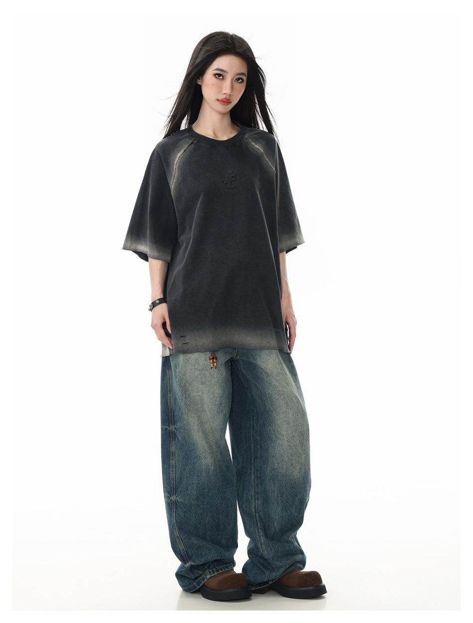Model wearing a charcoal oversized T-shirt with faded gray accents, paired with wide-leg blue jeans.