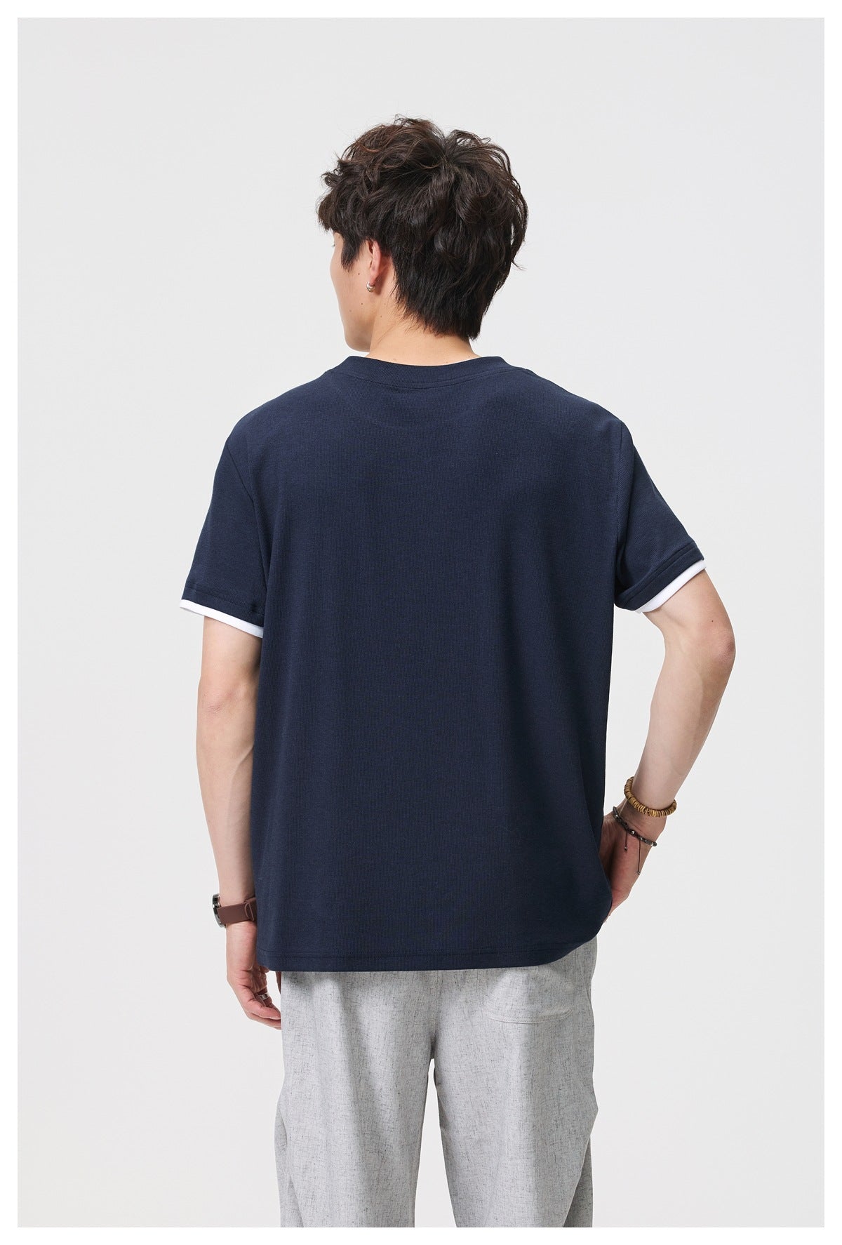 Back view of a model wearing a plain navy T-shirt with white trim beneath the sleeve cuffs.