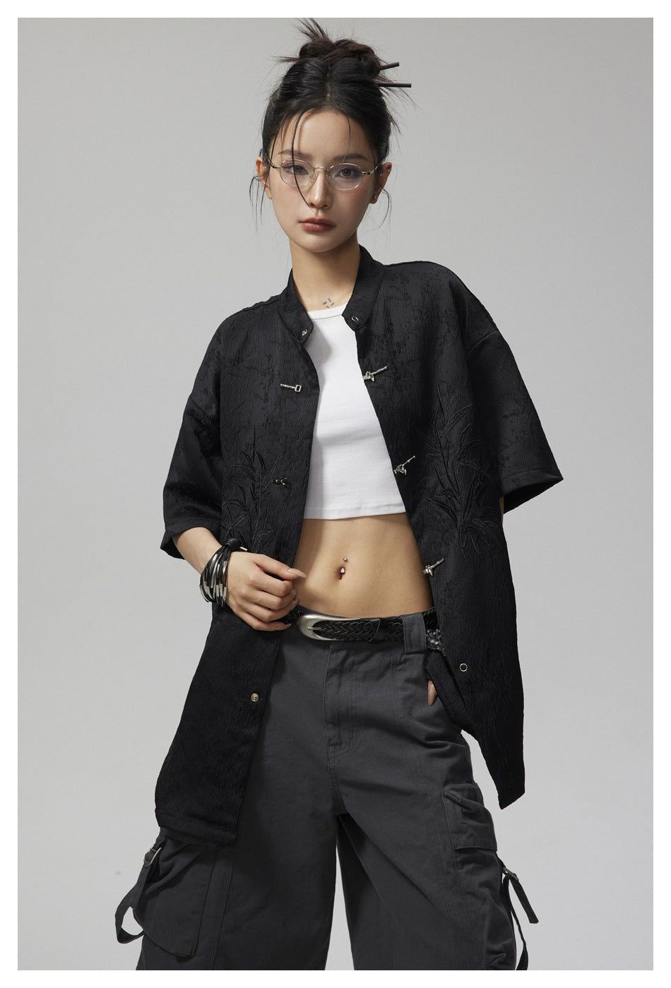 Model wearing an open black oversized jacket with short sleeves, metal frog closures and botanical embroidery.