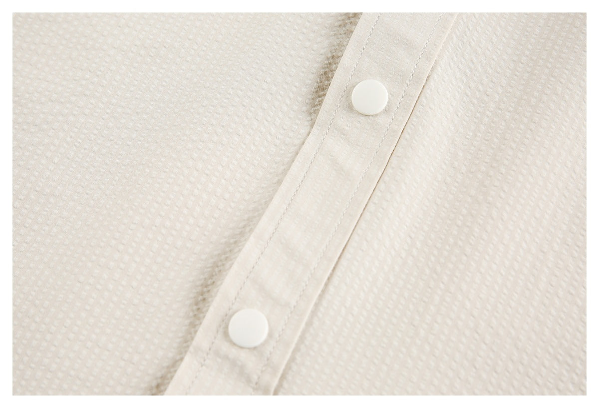 Close-up of an off-white textured garment's placket with two white snap buttons.