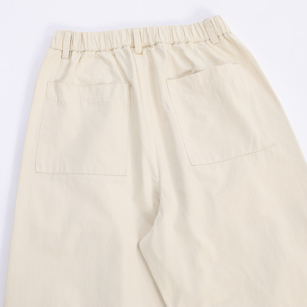 Back view of cream trousers with an elastic waistband and two large patch pockets.
