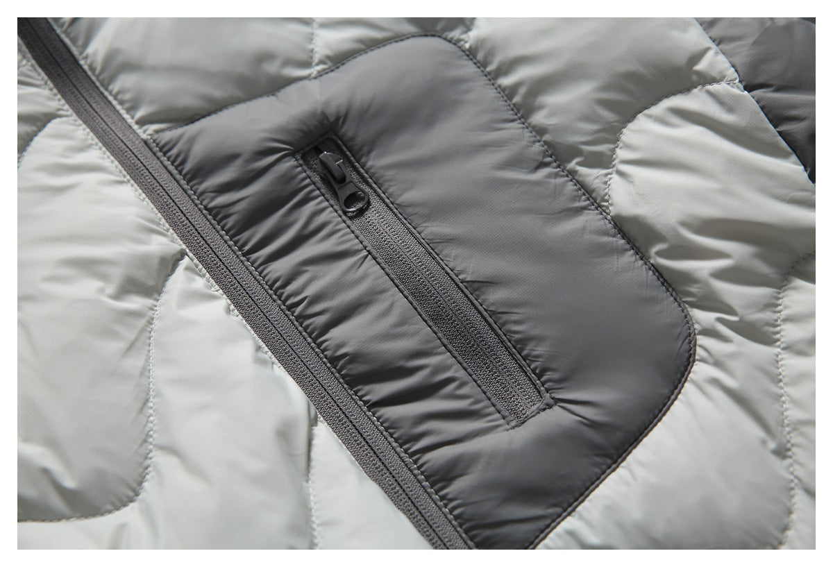 Close-up of a dark gray zippered pocket on the light gray quilted jacket front.