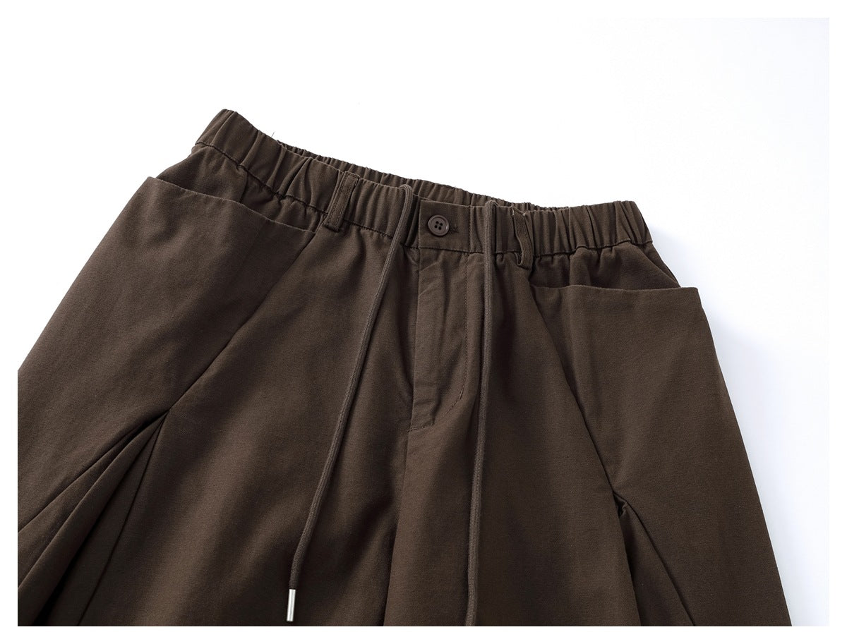 Front view of dark brown trousers with an elastic waist, drawstring, button closure, pleats and wide legs.