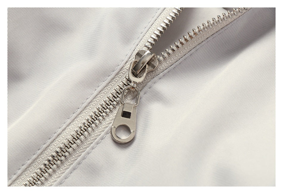 Close-up of a silver metal zipper and pull on light gray fabric, shown from the opposite side.