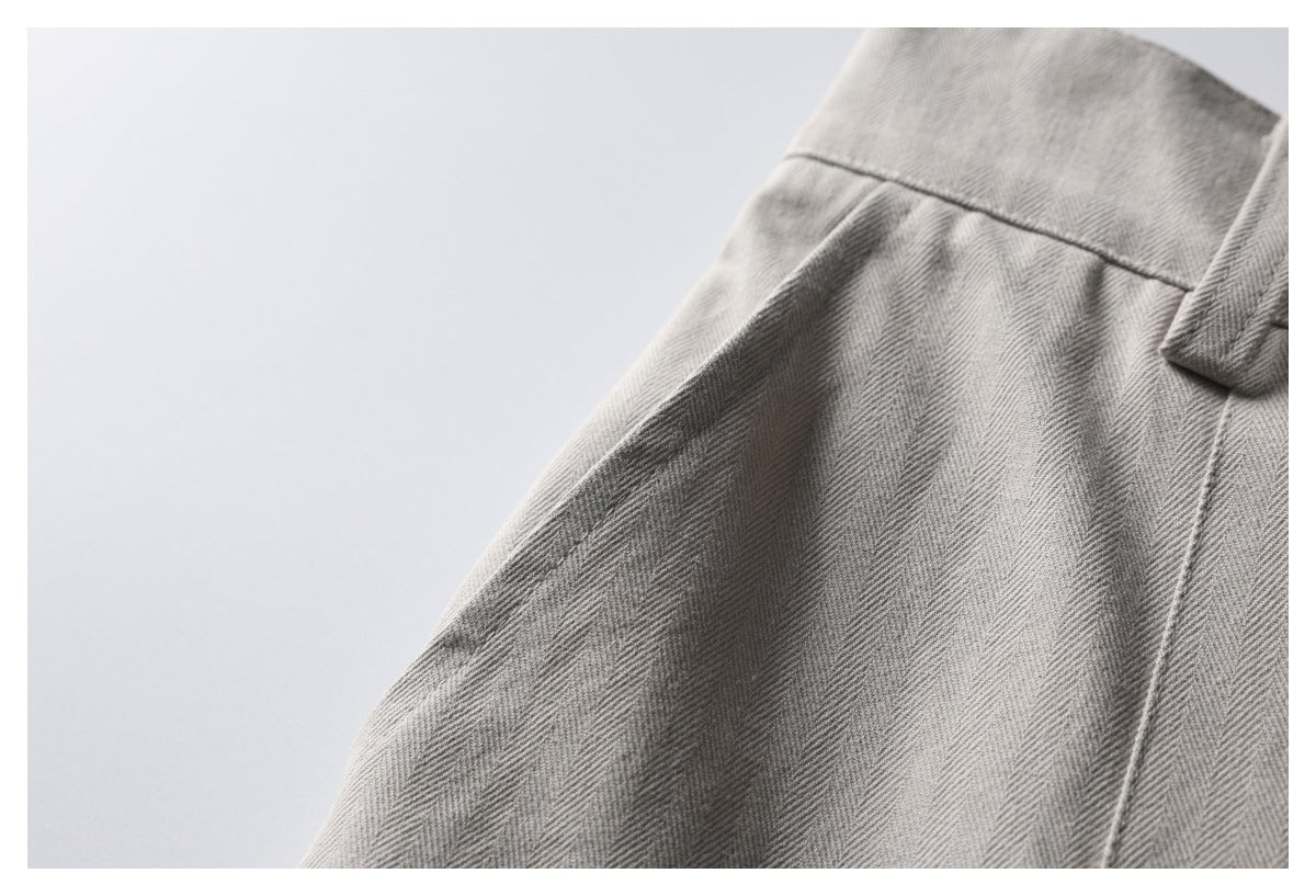 Close-up of the light gray herringbone fabric, waistband seam, and belt loop on the trousers.