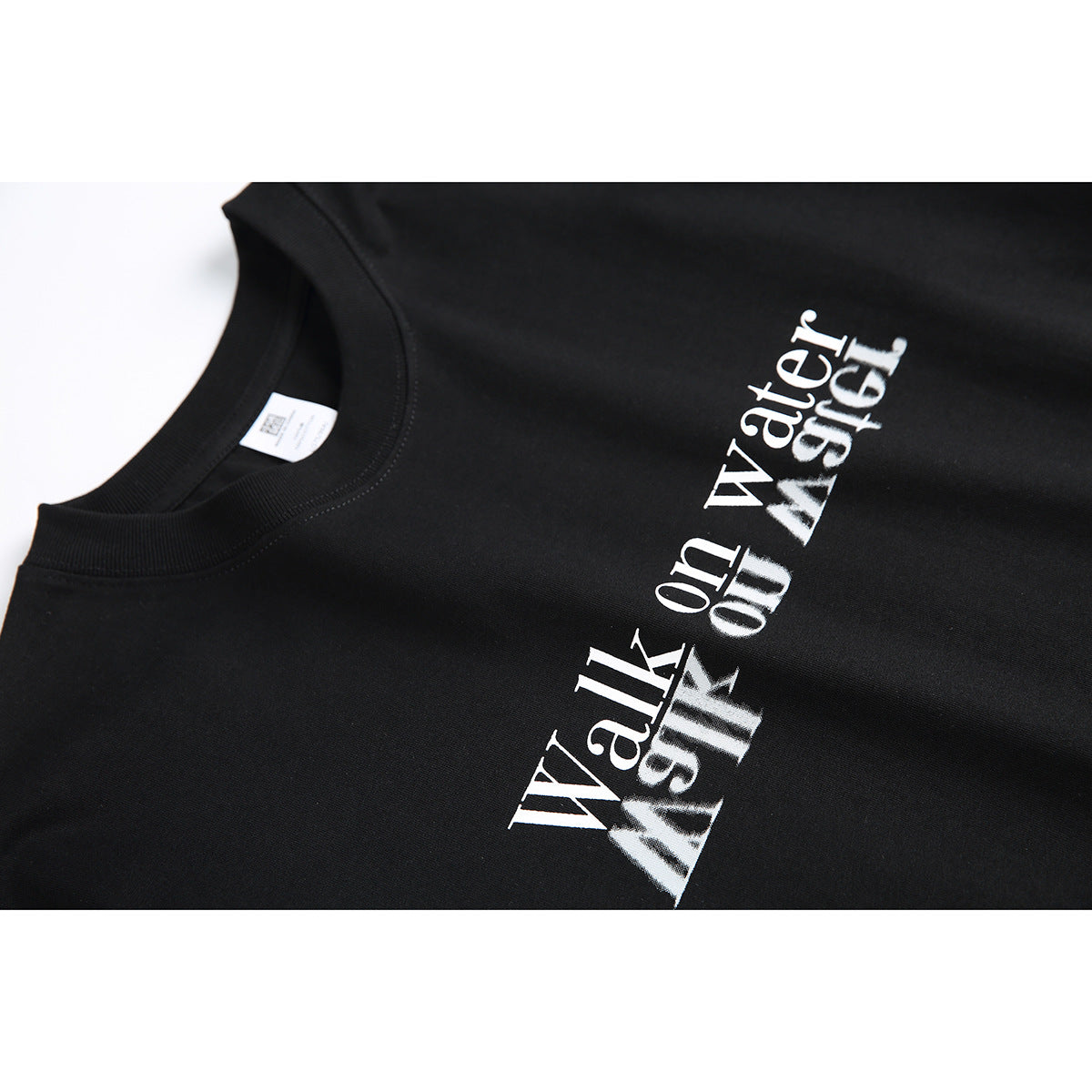 Angled close-up of the white “Walk on water” reflective text print on a black T-shirt.