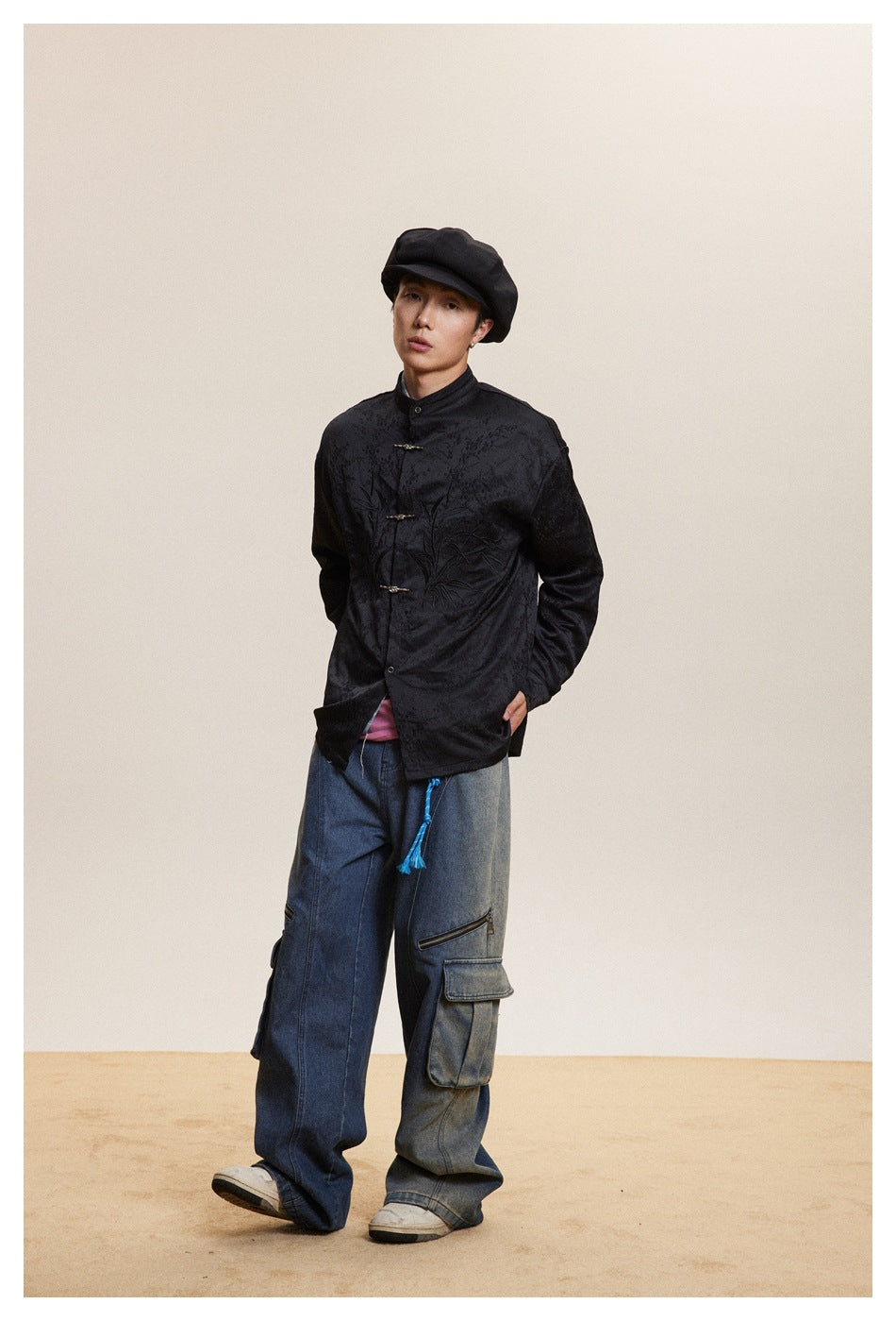 Model wearing a black embroidered stand-collar jacket with metal frog closures and loose blue cargo jeans.