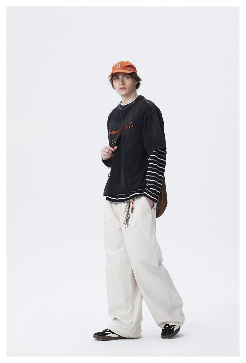 Model in a black graphic T-shirt layered over striped sleeves and loose white pants, shown in a three-quarter pose.