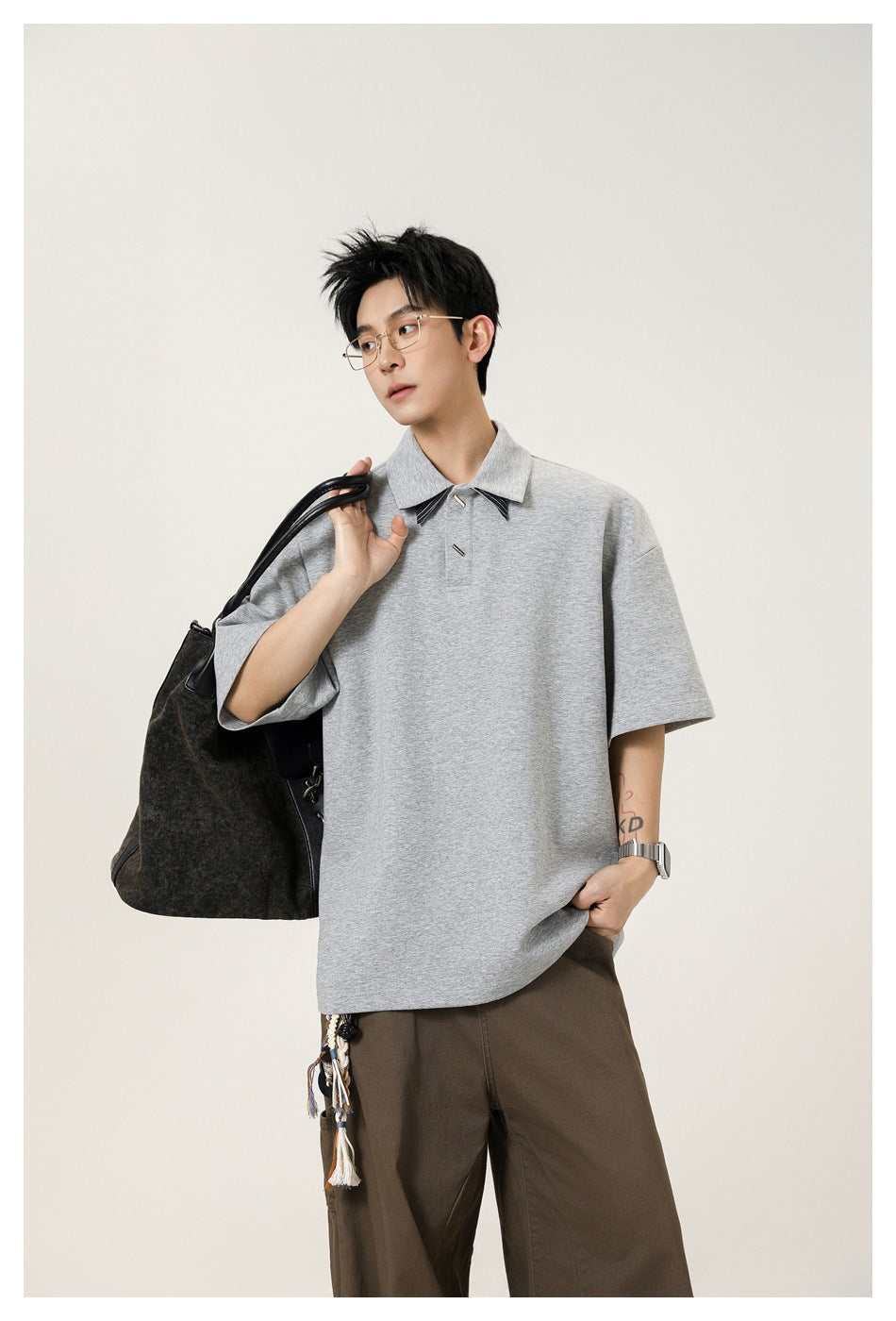 Model wearing an oversized light gray short-sleeve polo with a pointed collar and dark striped collar accents.