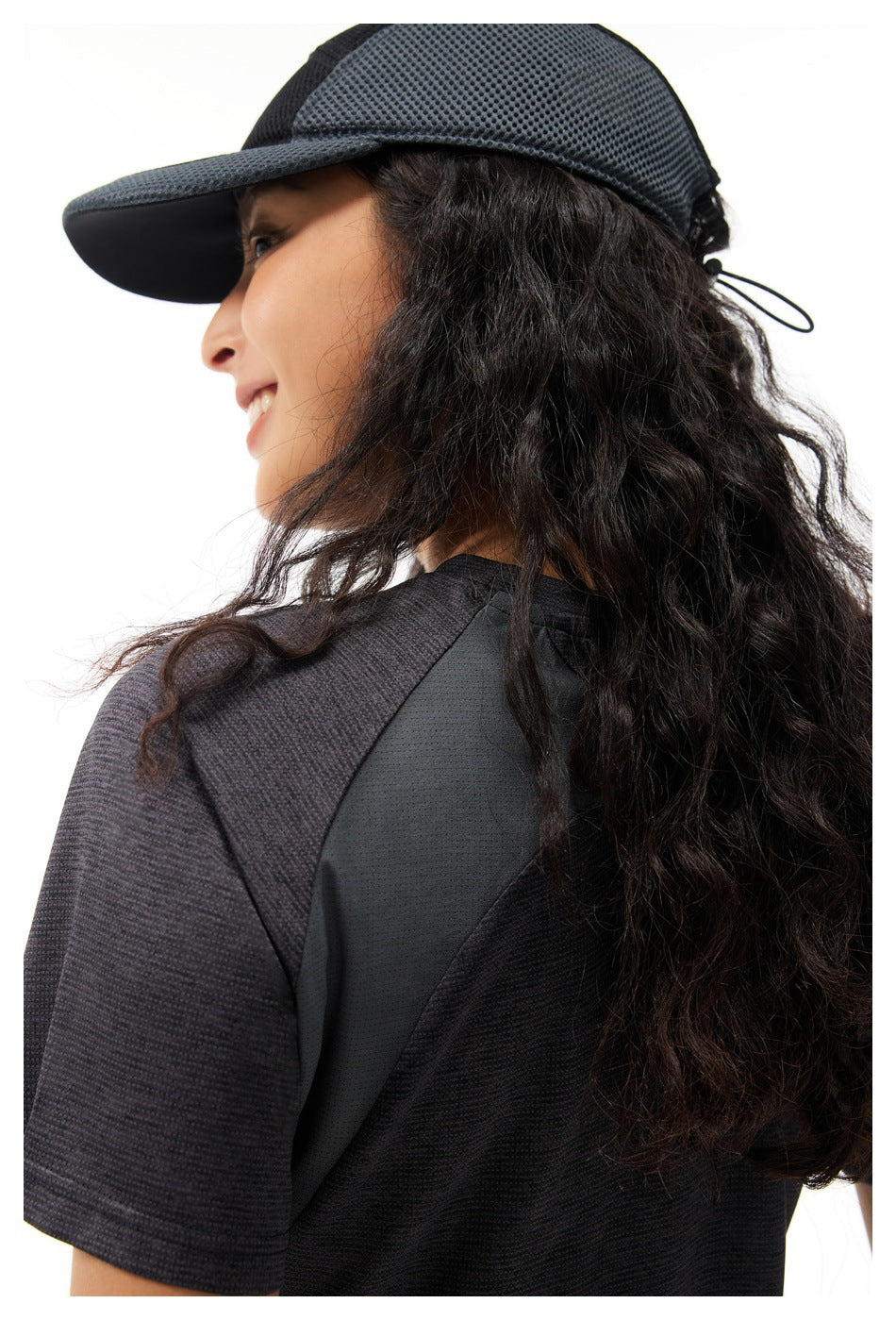 Close-up of the charcoal T-shirt's textured sleeve and dark mesh shoulder panel, with the model wearing a black cap.