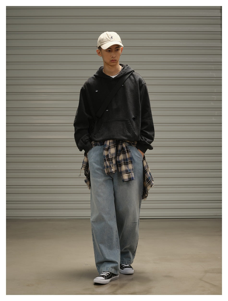 Front view of a model in a black distressed hoodie and loose blue jeans, with a plaid shirt tied around the waist.