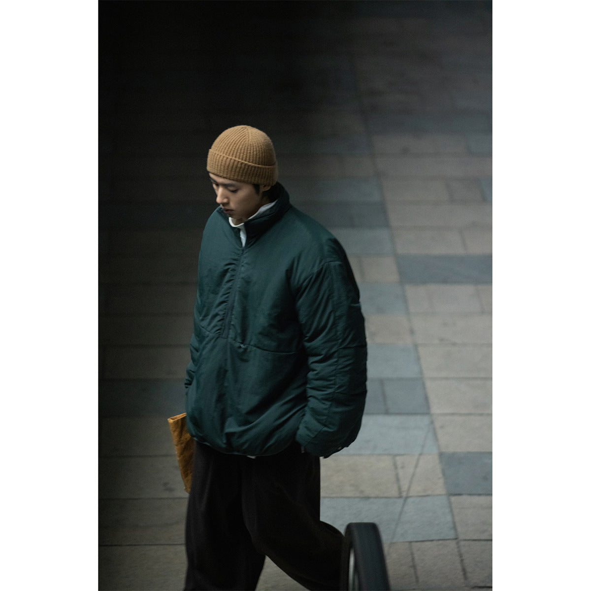 Model wearing a dark teal padded pullover jacket with a high collar and a tan knit beanie.
