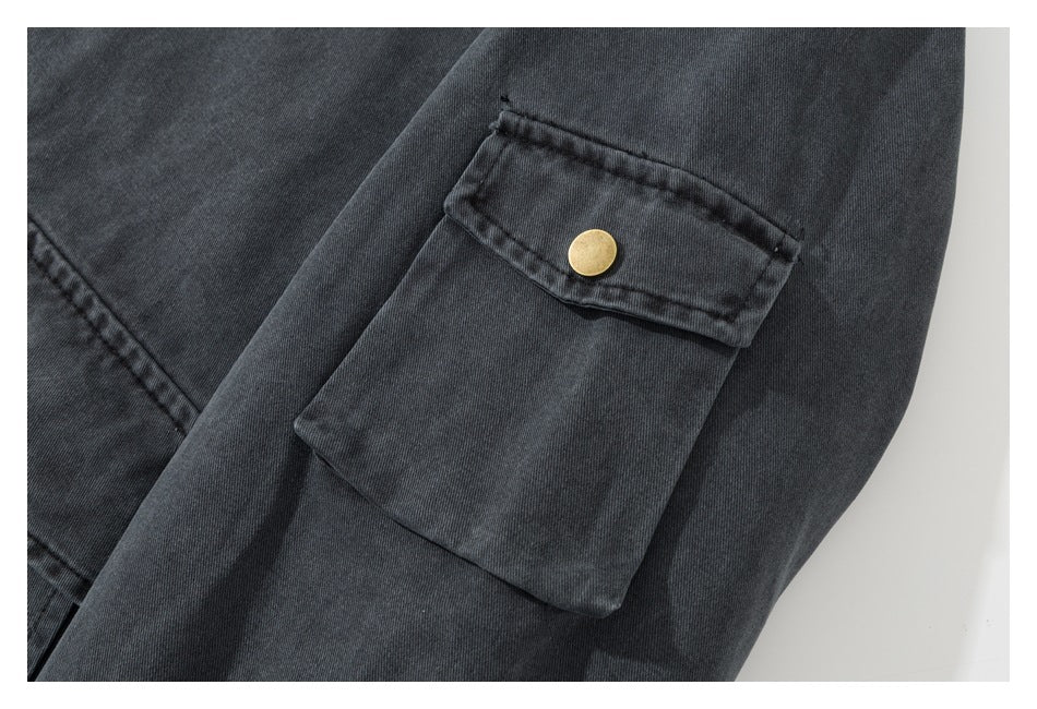Close-up of a charcoal jacket sleeve pocket with a brass snap flap.