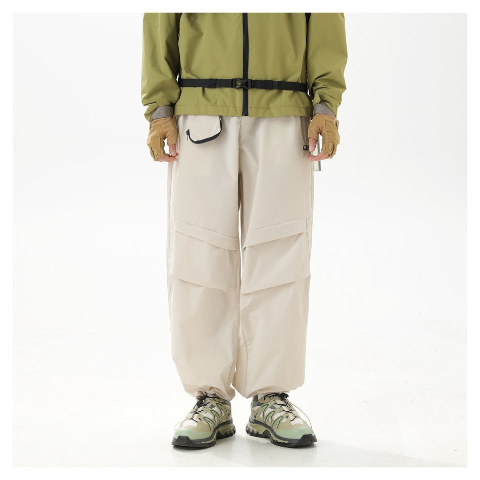 Front view of a model wearing loose ivory trousers with large layered knee panels and a black-trimmed pocket.