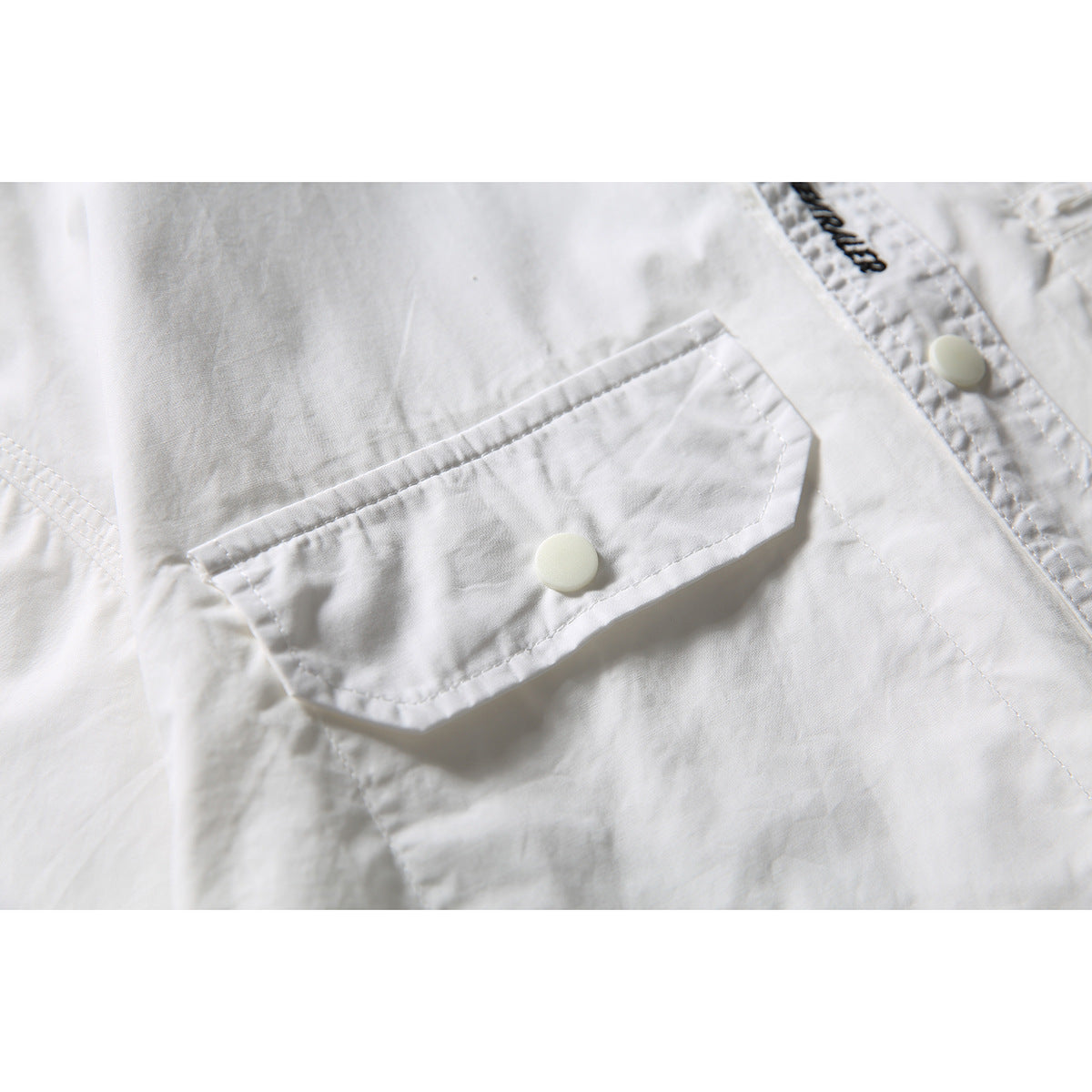 Close-up of the white shirt's flap chest pocket, snap button, stitching and part of the front placket.