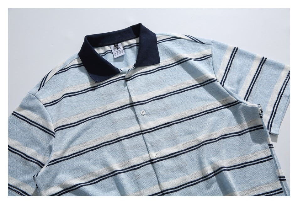 Partial flat-lay front of a pale blue and white striped polo with a navy collar and short sleeves.