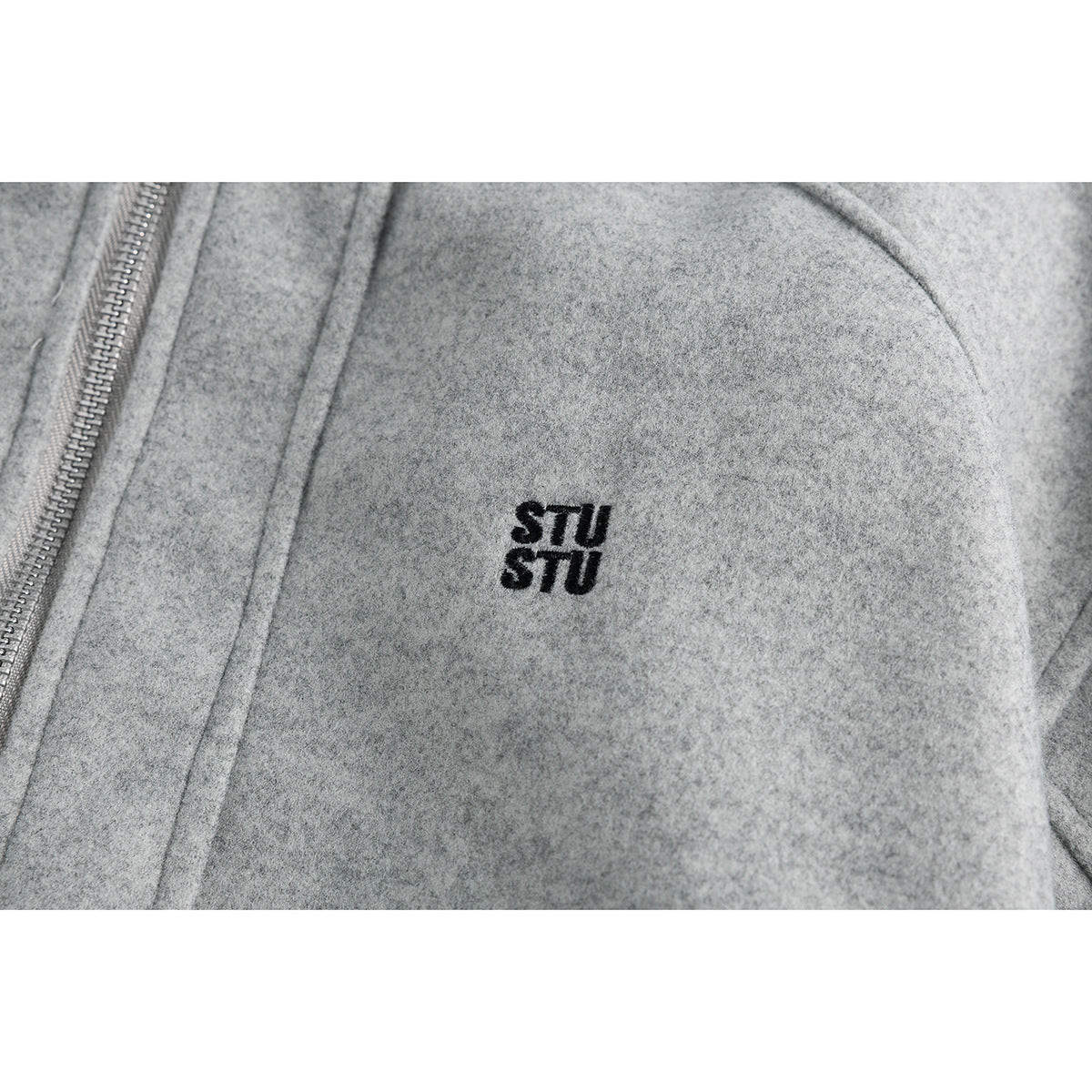 Close-up of a small black STU logo embroidered on the chest of a gray jacket.