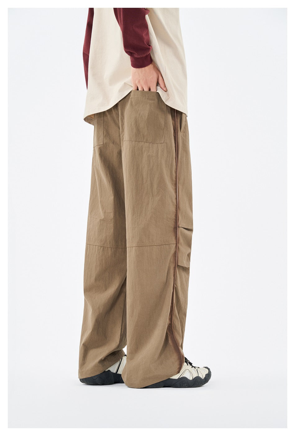 Side and rear view of a model wearing loose tan trousers with a large back pocket and contrast side piping.