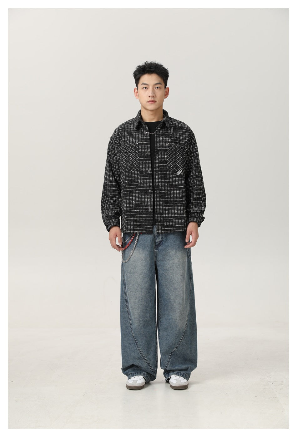 Model wearing a black grid-check shirt-jacket open over a black tee with wide-leg blue jeans and a chain