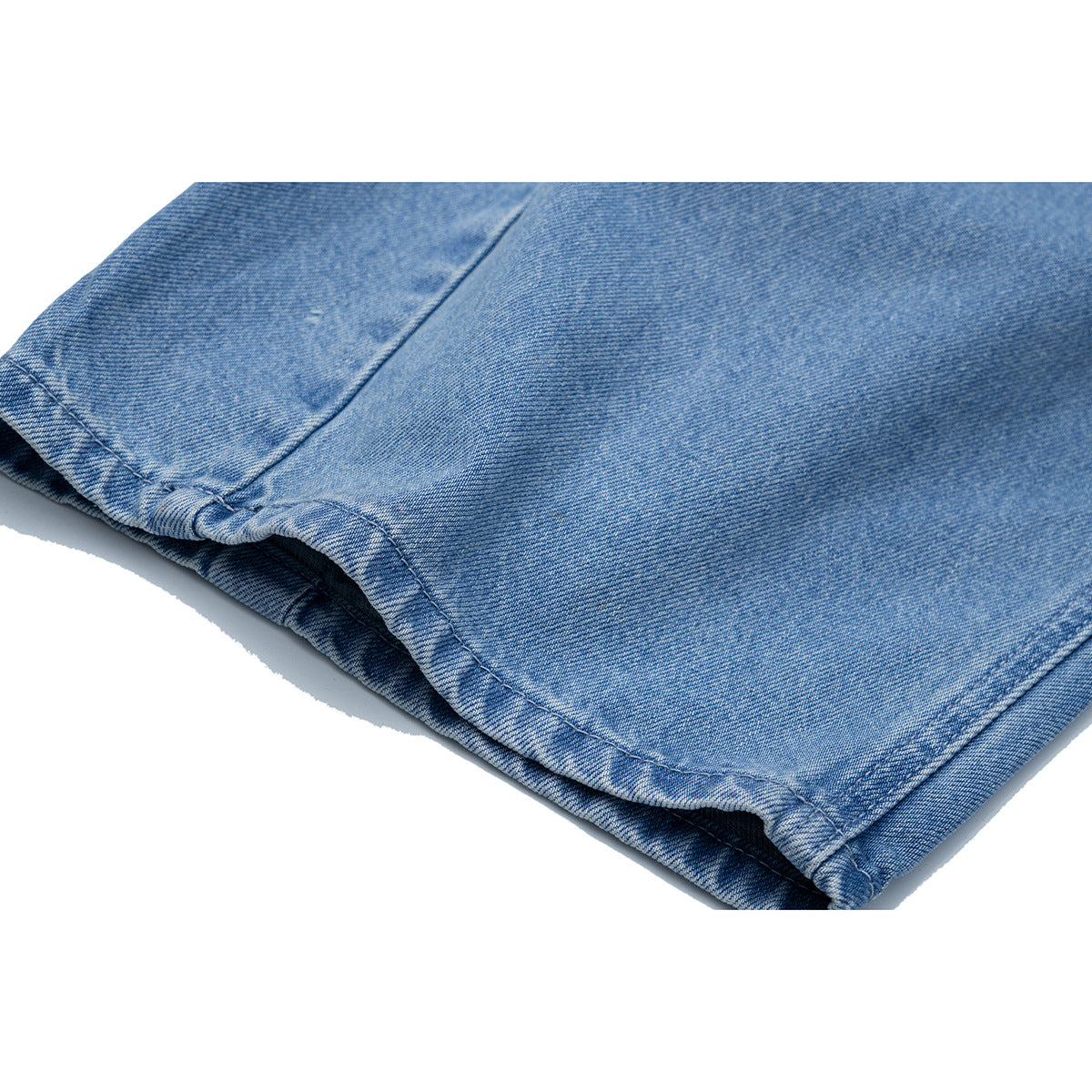 Close-up of the stitched hem and leg opening of light blue jeans.