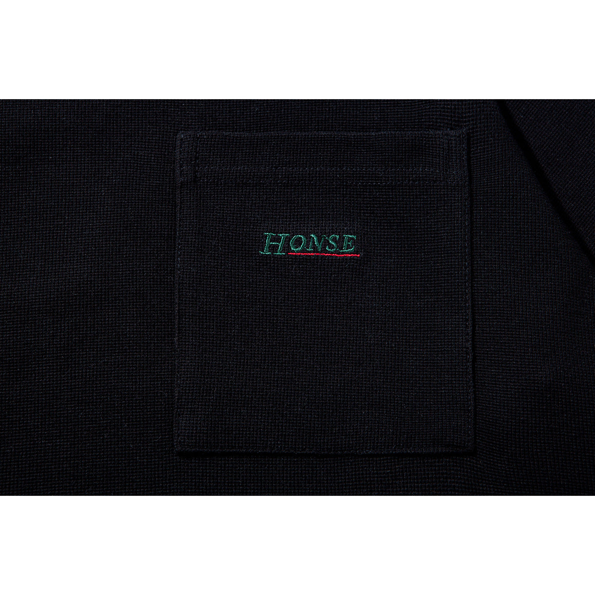 Close-up of a black T-shirt chest pocket with small green and red embroidered lettering.
