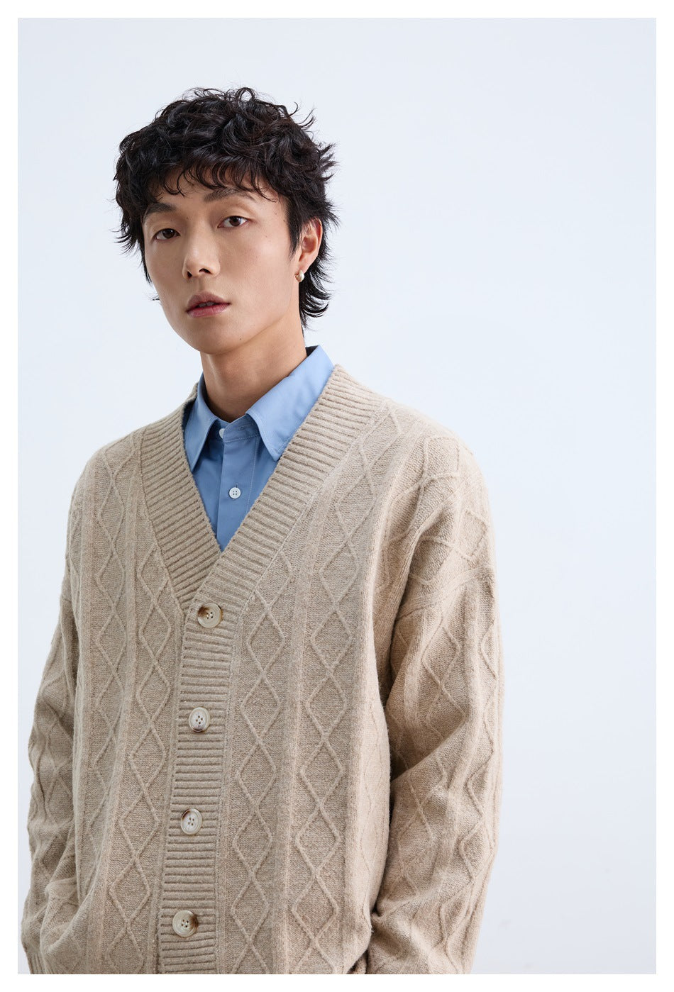 Close view of a model wearing a beige diamond cable-knit cardigan over a light blue shirt.