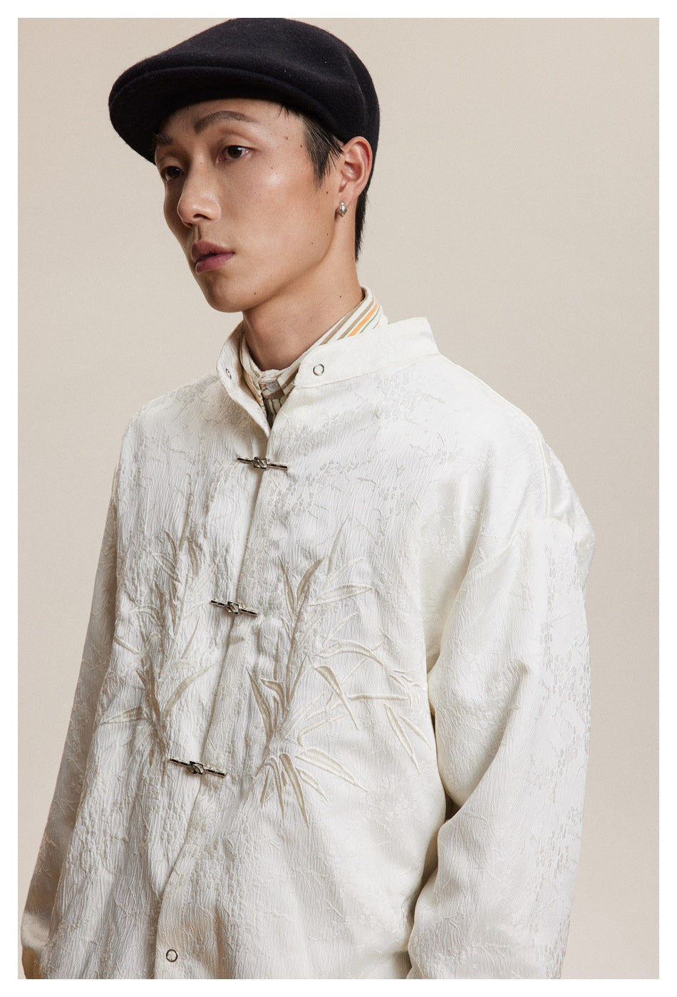 Close view of an ivory jacket with raised bamboo embroidery, a stand collar, and metal frog closures.