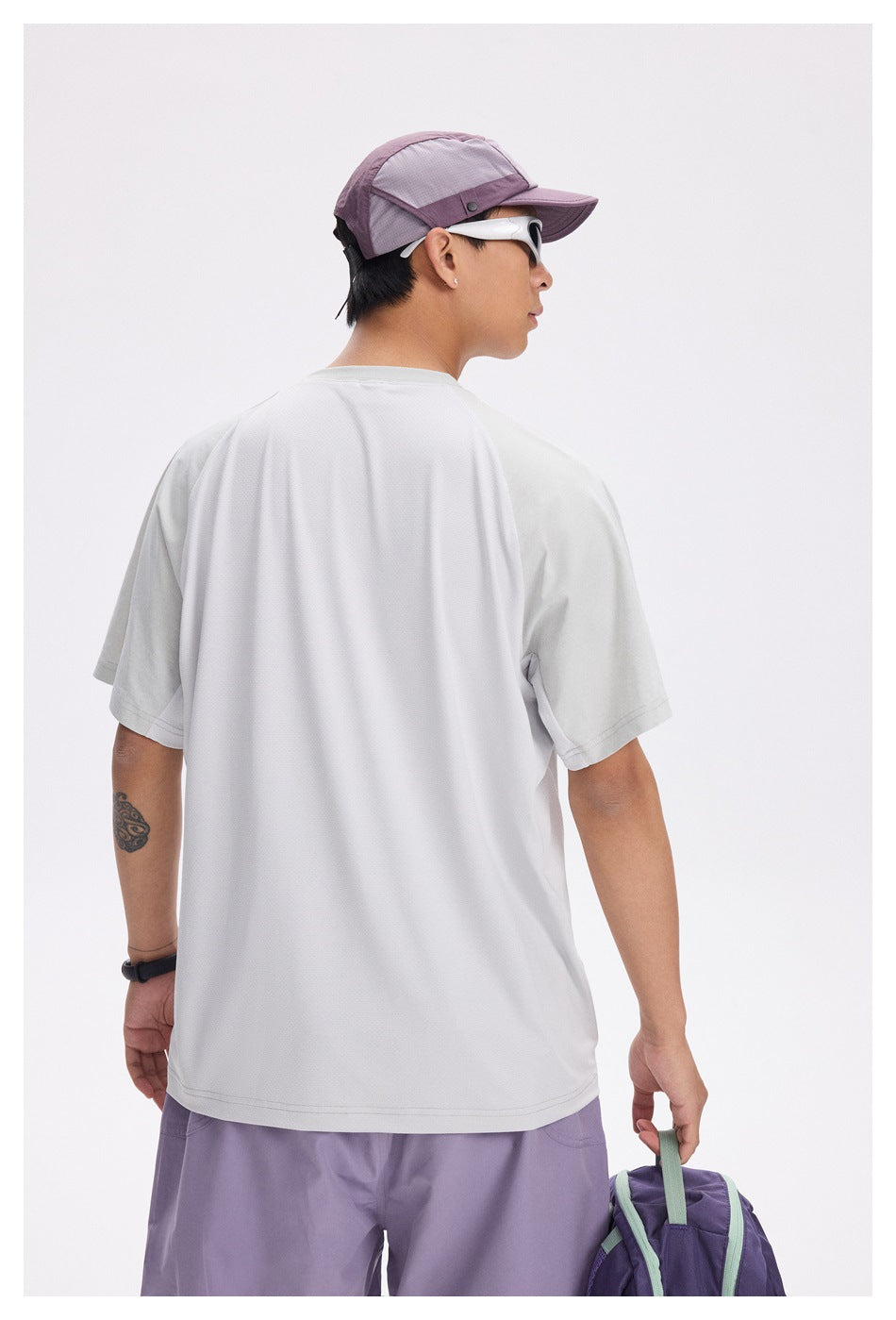 Rear view of a man wearing a plain light gray short-sleeve T-shirt with lavender shorts and a mauve cap.