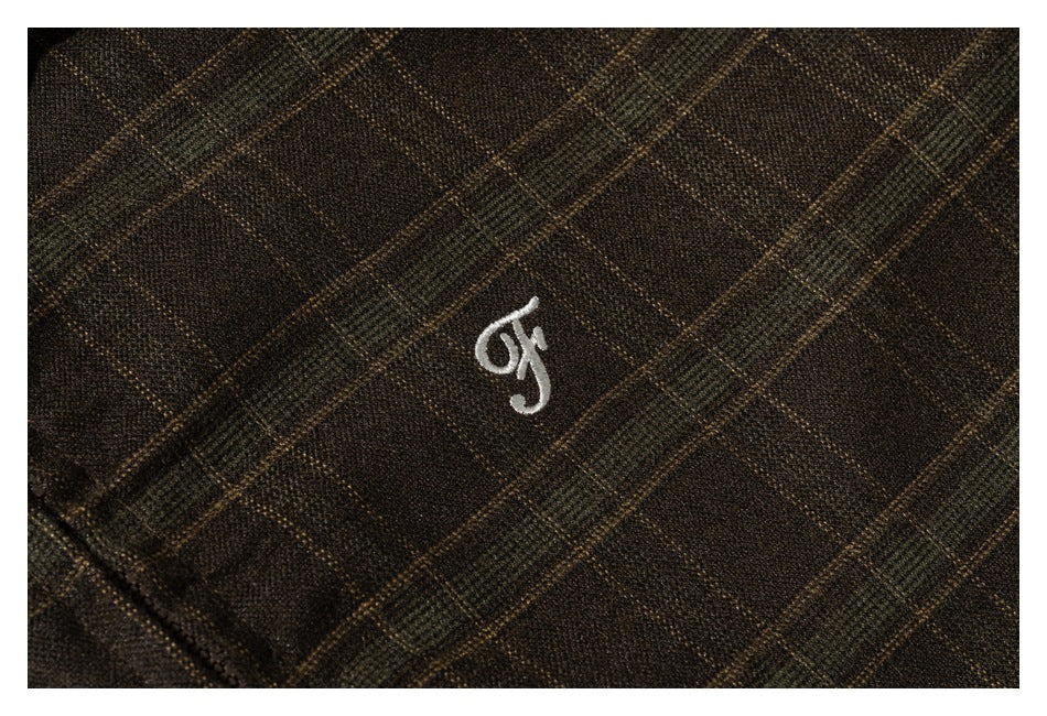 Close-up of brown plaid fabric with a small white embroidered mark.