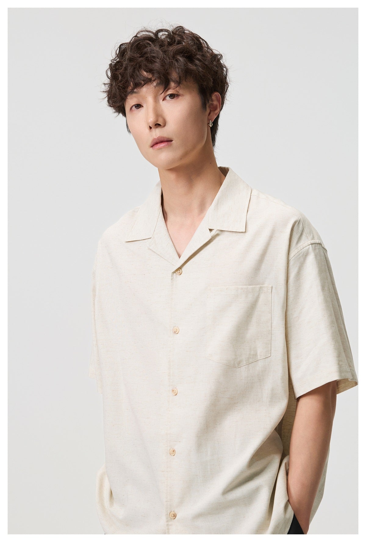 Close front view of a male model wearing an off-white short-sleeve shirt with an open collar and chest pocket.