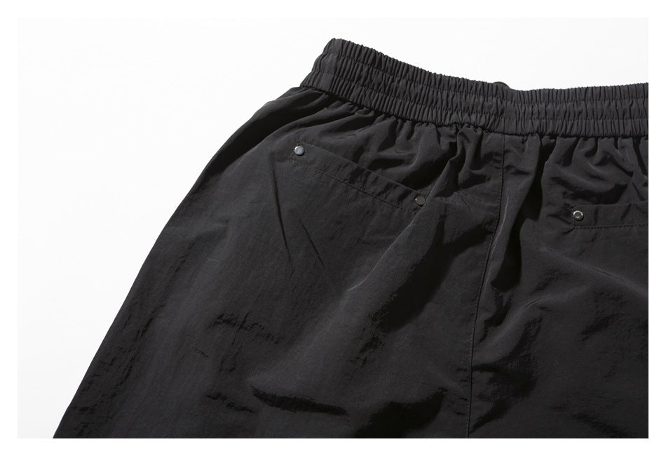 Close-up of the back waistband and two snap-trimmed pockets on black shorts.