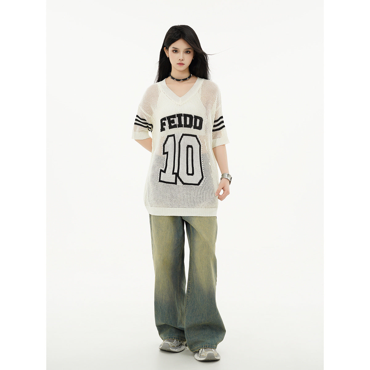 Model wearing an ivory mesh V-neck jersey tunic with black sleeve stripes and FEIDD 10 lettering, styled with wide-leg jeans.