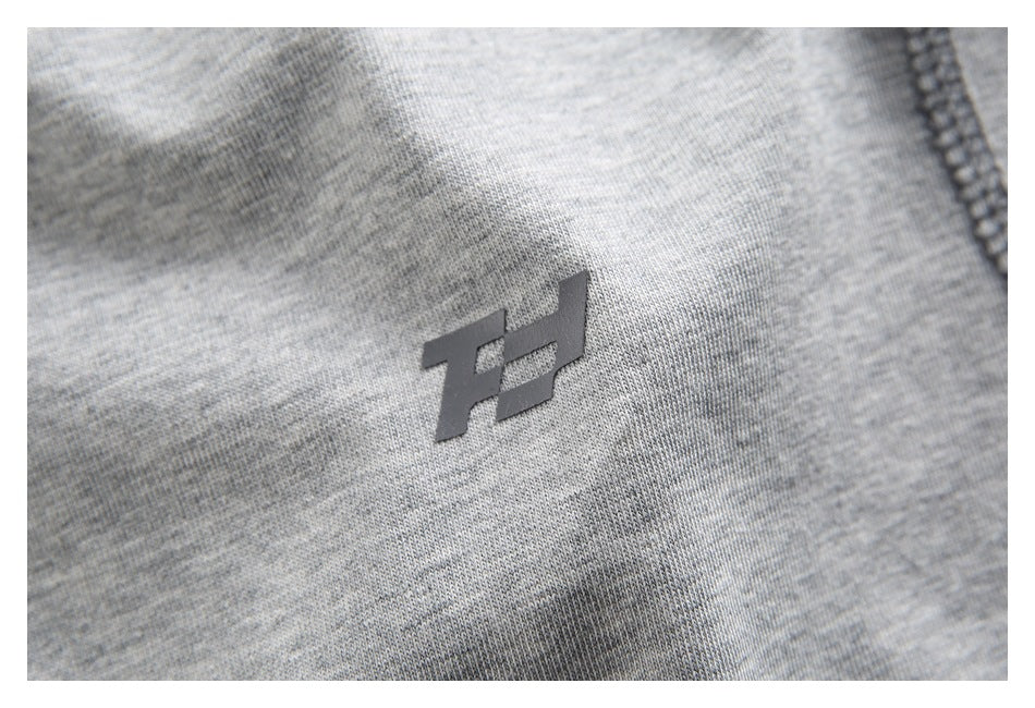 Close-up of a small dark geometric logo on heather-gray shirt fabric.