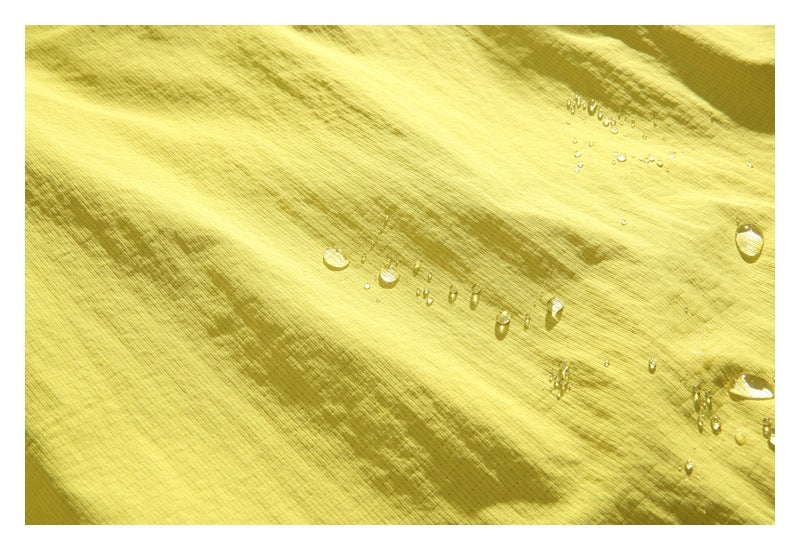 Water droplets bead on the textured yellow-green jacket fabric.