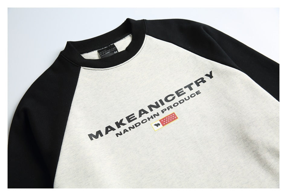 Close-up of an off-white and black raglan sweatshirt chest with bold black lettering and a small red-and-yellow graphic.