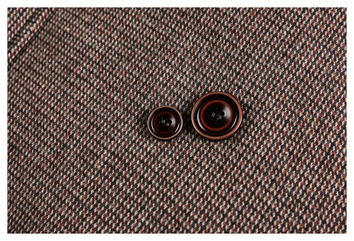 Close-up of two dark brown buttons against the coat's brown, cream, and rust patterned fabric.