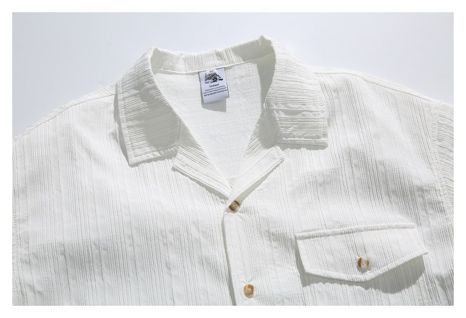 Close-up of a white short-sleeve shirt with a notched collar, tan buttons, flap chest pocket, and raised vertical stripes.