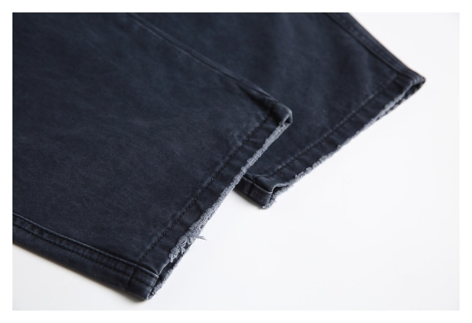 Close-up of a dark charcoal jeans leg ending in a raw, frayed hem.