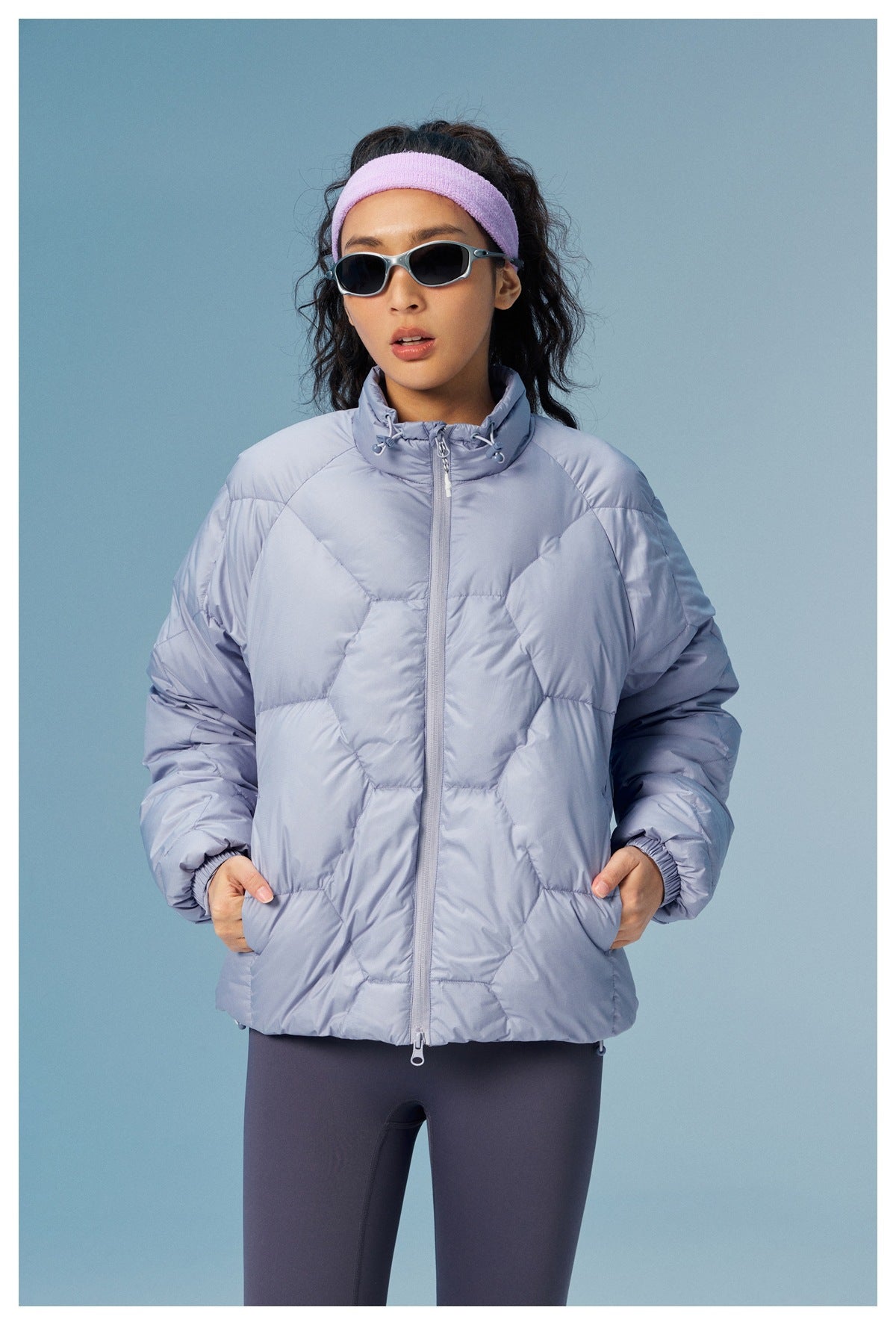 Front view of a model wearing a pale lavender quilted jacket with a high drawcord collar and zip pockets.