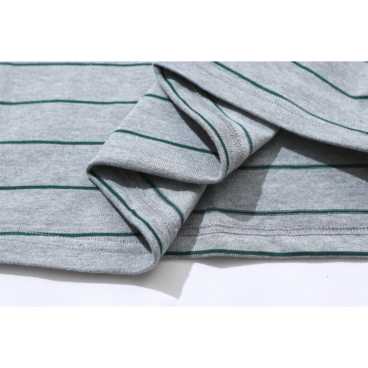 Close-up of the stitched hem and folded edge of a gray T-shirt with thin dark green stripes.