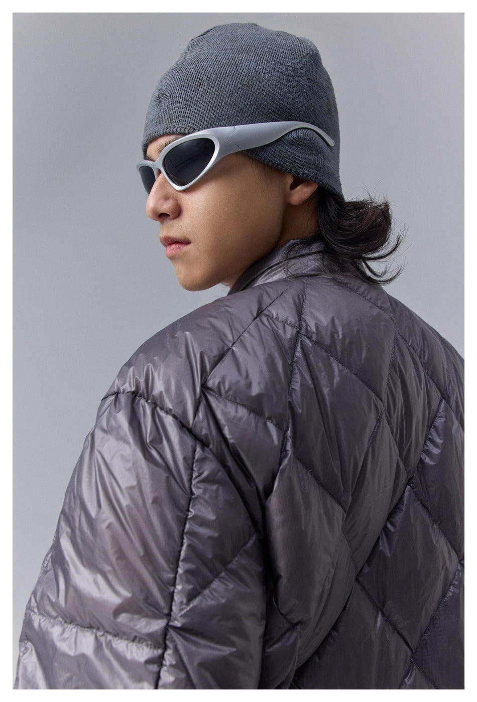 Close-up side view of a model in a glossy charcoal quilted jacket and gray knit beanie.