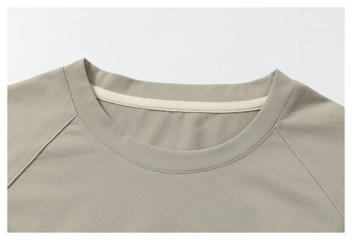 Close-up of the light taupe T-shirt's ribbed crew neckline and raglan shoulder seams.