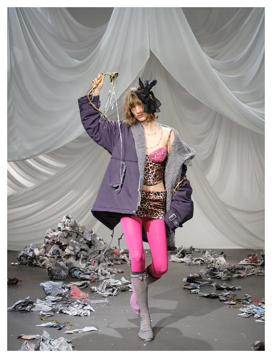 Full-length runway view of a model in a deep plum parka with gray trim, bright pink leggings and a leopard-print outfit.