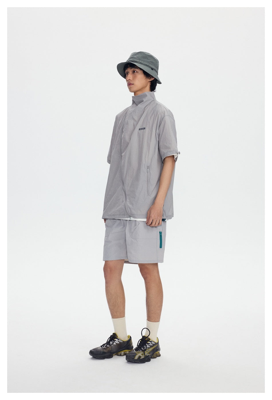 Model in gray short-sleeve stand-collar zip jacket with gray shorts, bucket hat and sneakers, side view