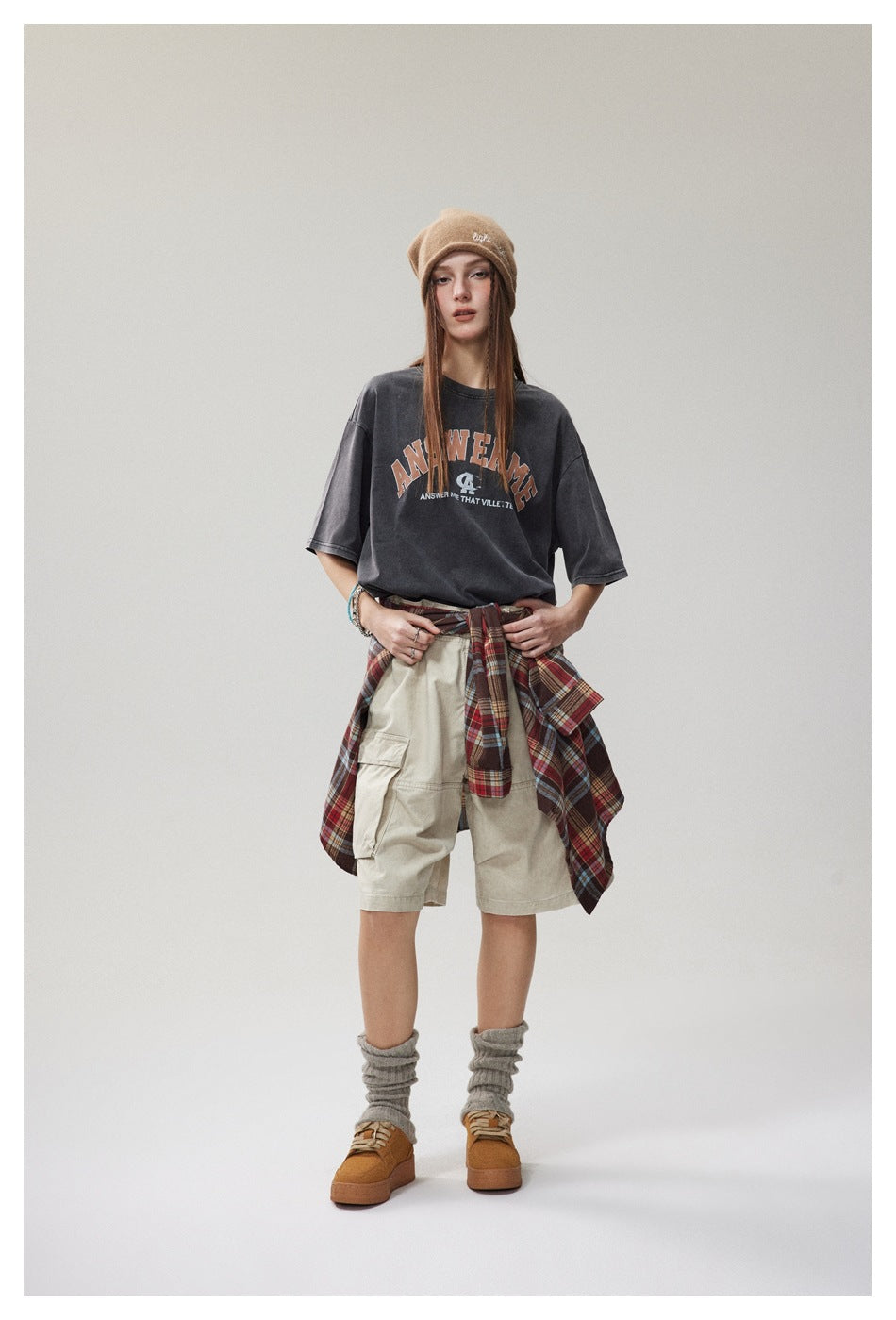 Model wearing washed black ANSWERME T-shirt with beige cargo shorts, tied plaid shirt, beanie and boots