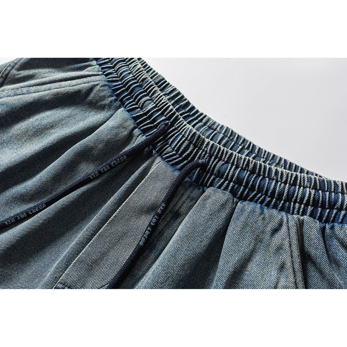 Close-up of blue denim shorts showing the gathered elastic waistband and stitched seams.